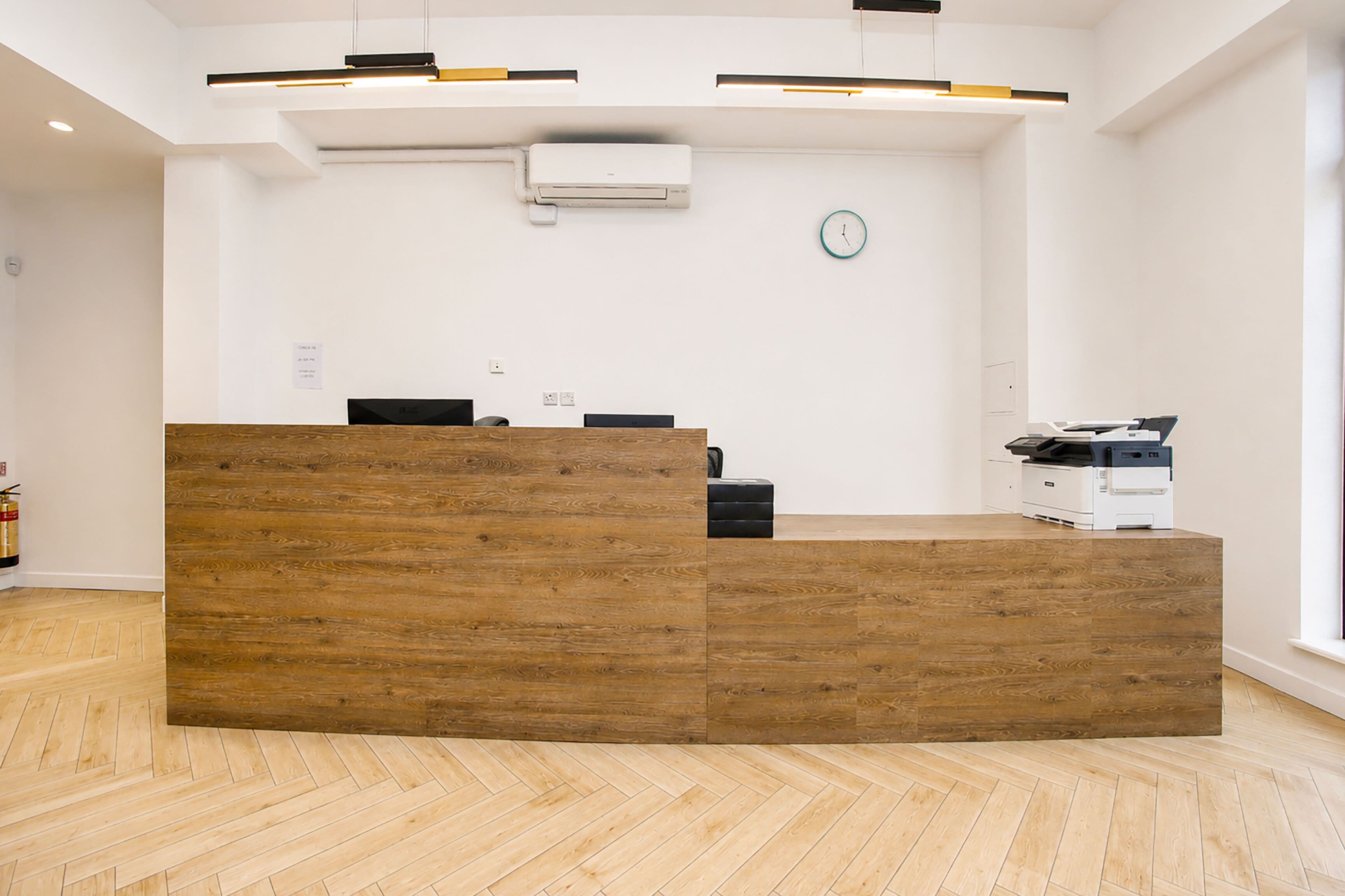 A reception desk with a wooden finish, a clock on the wall, and a fire extinguisher in the corner.