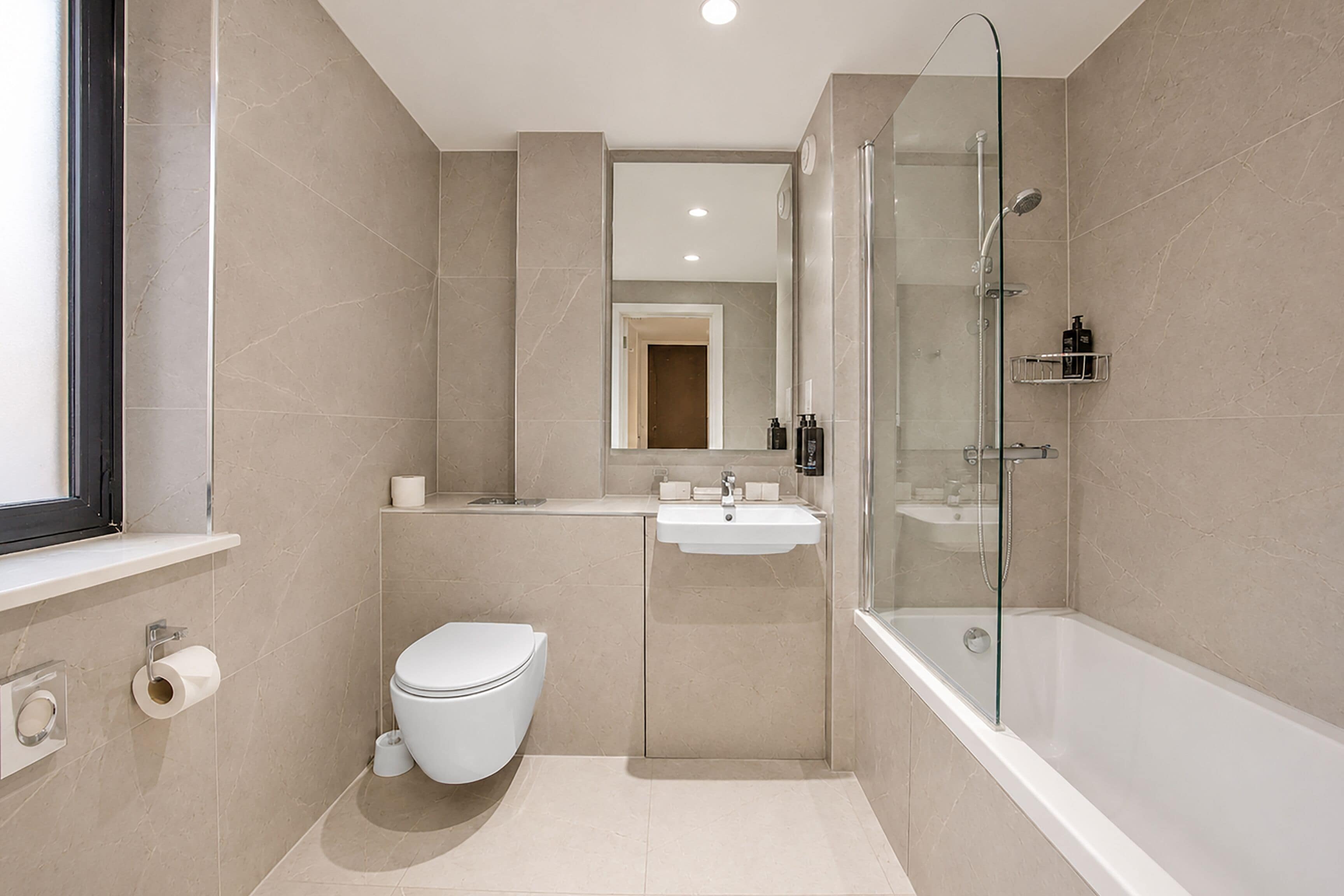 Un baño moderno con inodoro, lavamanos y ducha con mampara de vidrio.