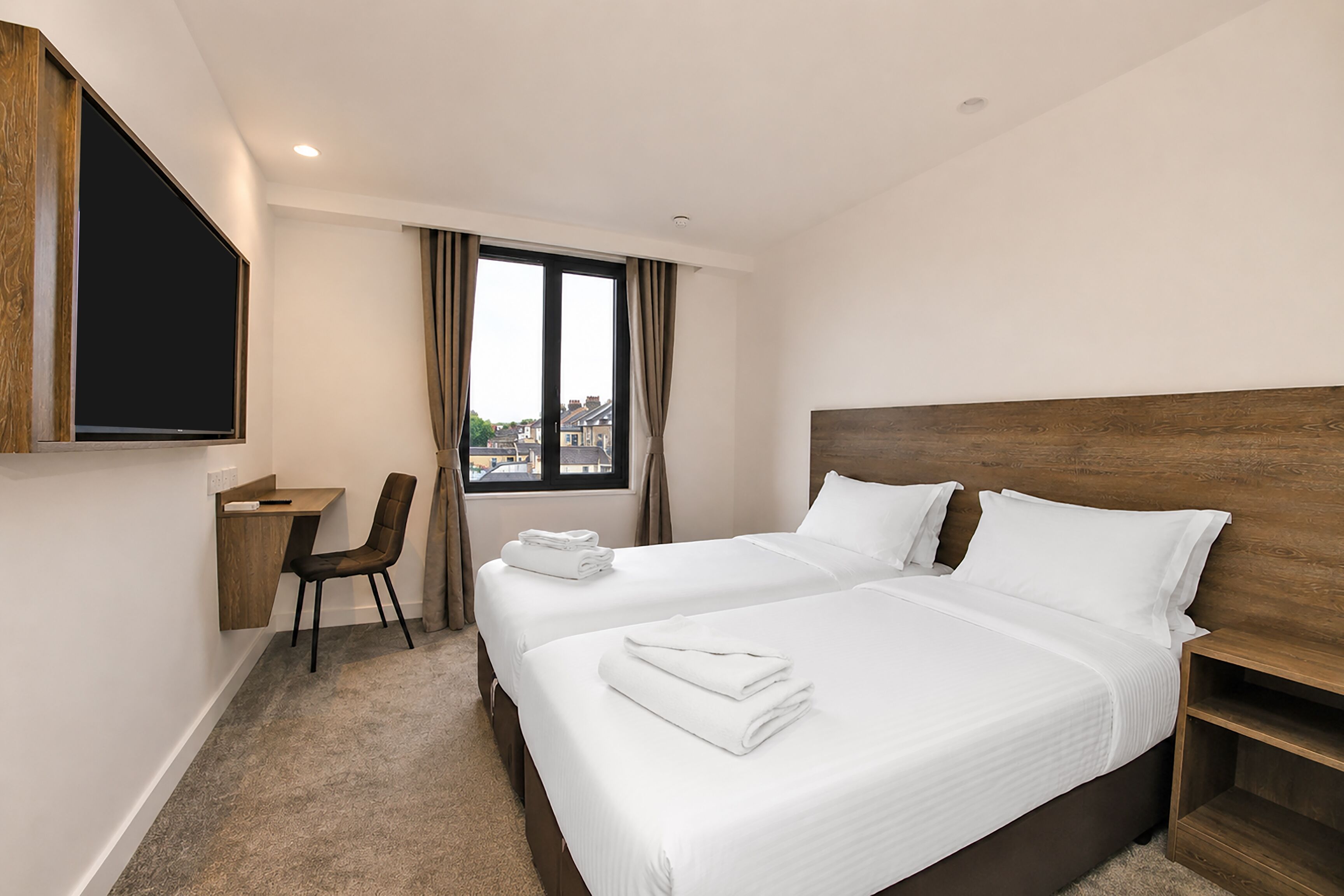 A hotel room with two beds, a desk, a chair, and a TV.