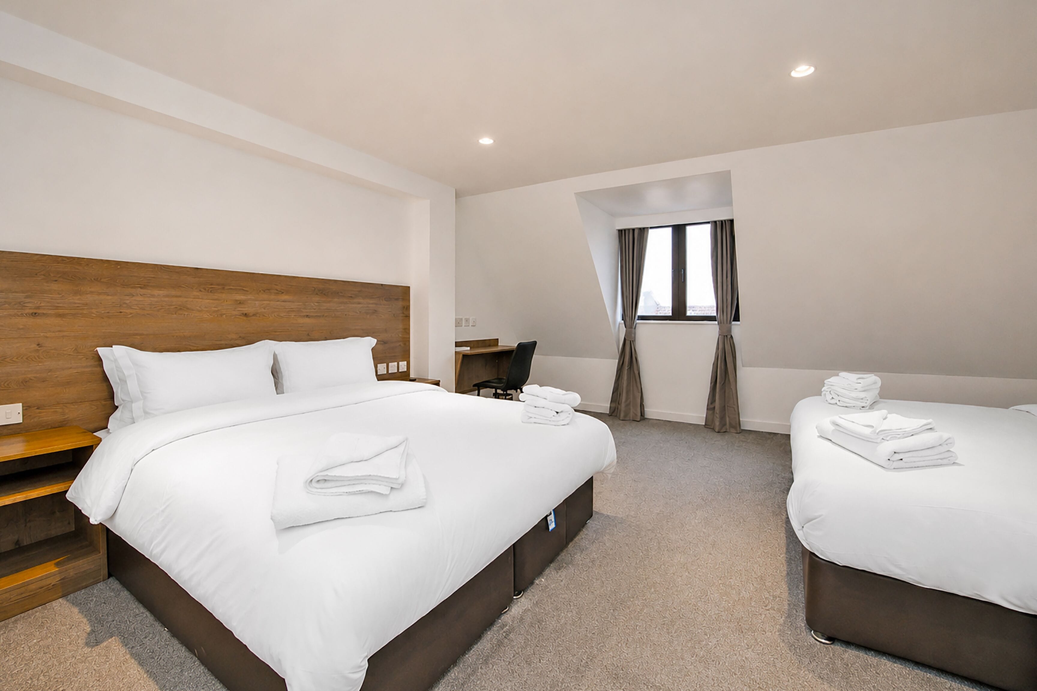 A hotel room with a large bed, a smaller bed, a desk, and a window with curtains.