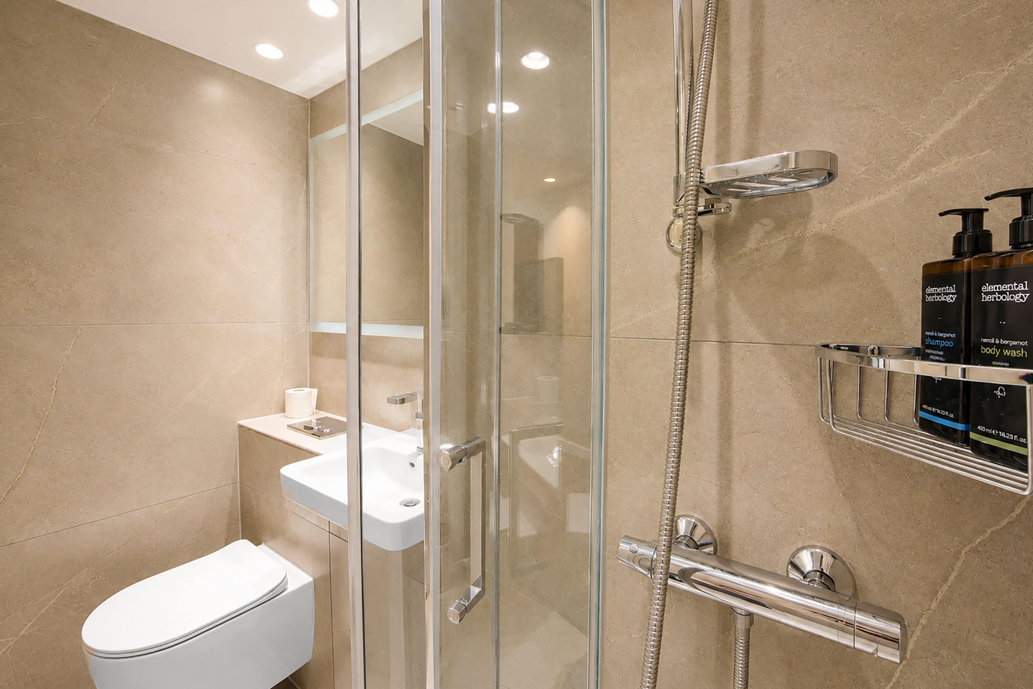 Een moderne badkamer met een douche met glazen wand, een wit toilet en een wastafel met spiegel.