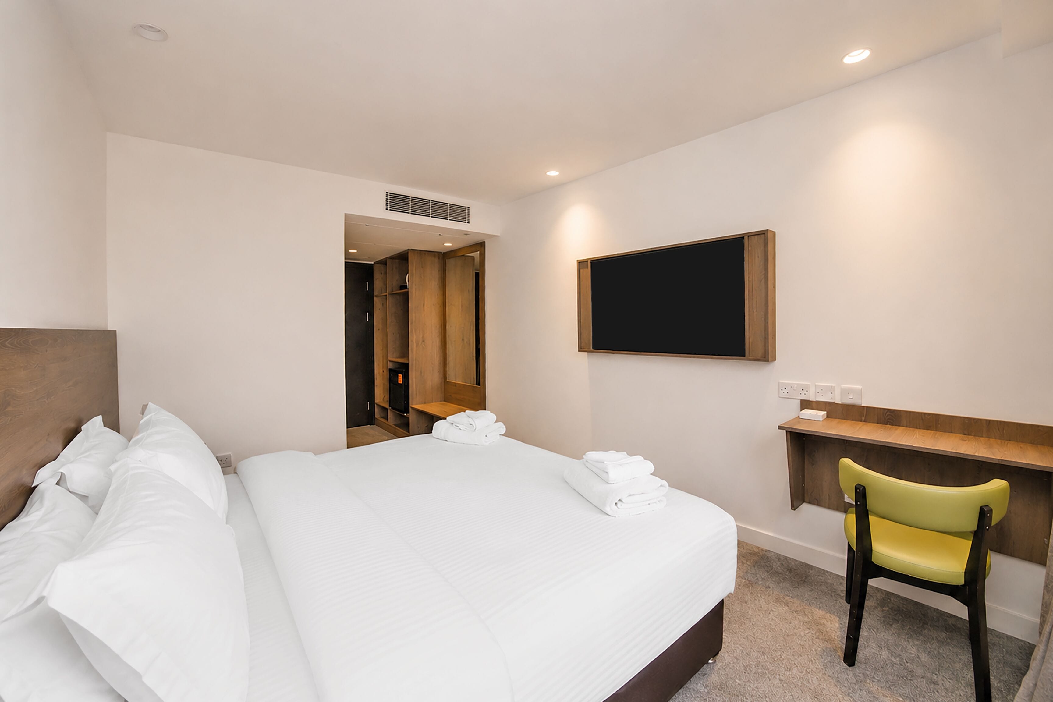 A hotel room with a large bed, a desk, a chair, and a flat-screen TV mounted on the wall.