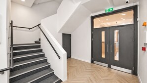 Una escalera con barandilla, suelo con diseño de espiga y una puerta con letrero de salida verde.