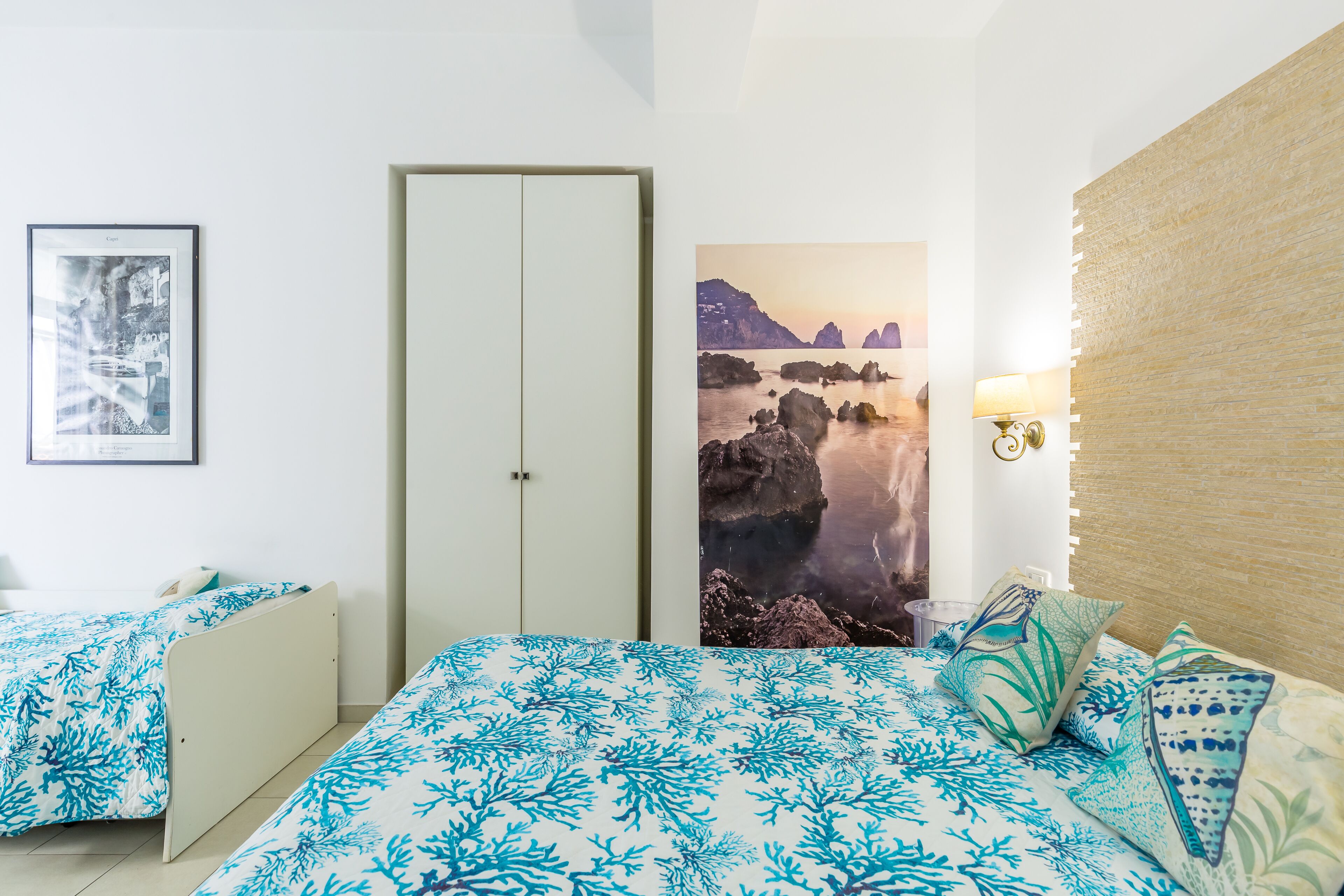 A bedroom with two beds, a door, a wall-mounted lamp, and a framed picture.