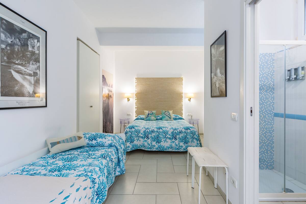 Habitación de hotel con dos camas, una mesita, zona de ducha y obras de arte en las paredes.
