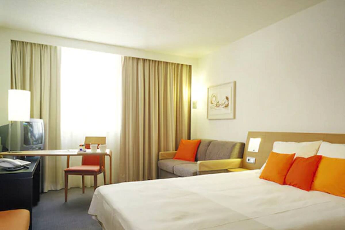 A hotel room with a large bed, a desk with a chair, a television, and a window with curtains.
