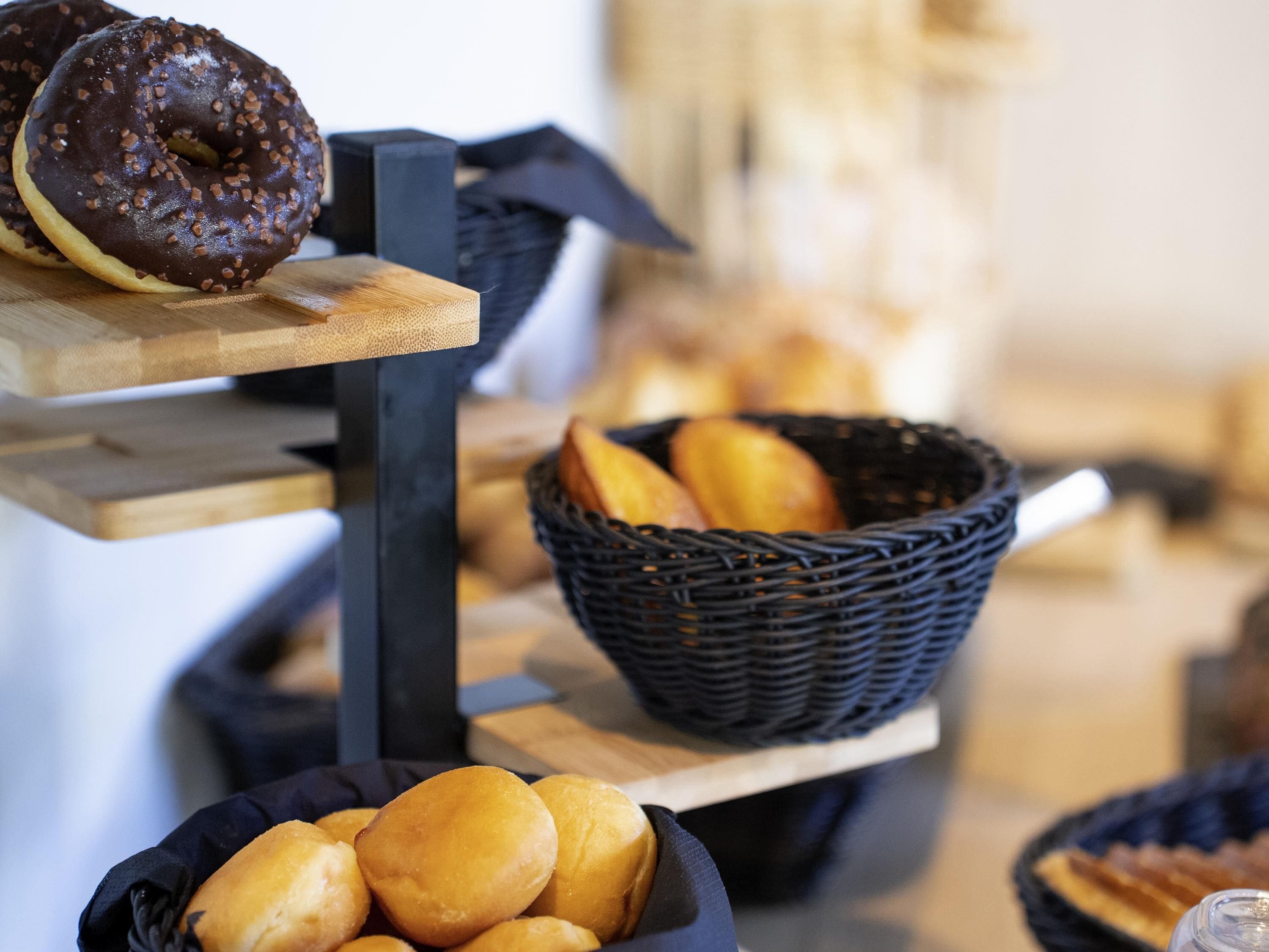 A bakery display with chocolate and plain doughnuts, a basket of bread, and a wooden serving board.