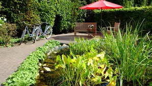 A garden with a pond, a bench, and a bicycle. - Hotel An der Gruga (Essen)