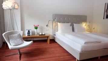 A hotel room with a bed, a chair, a bedside table, a lamp, and a floor lamp.