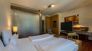 A hotel room with a bed, a desk, a television, and a painting on the wall. - Hotel An der Gruga (Essen)