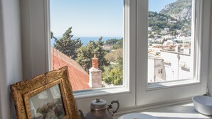 Una ventana con vistas a un pueblo costero, un cuadro enmarcado, un hervidor de agua, una taza y un plato con galletas.