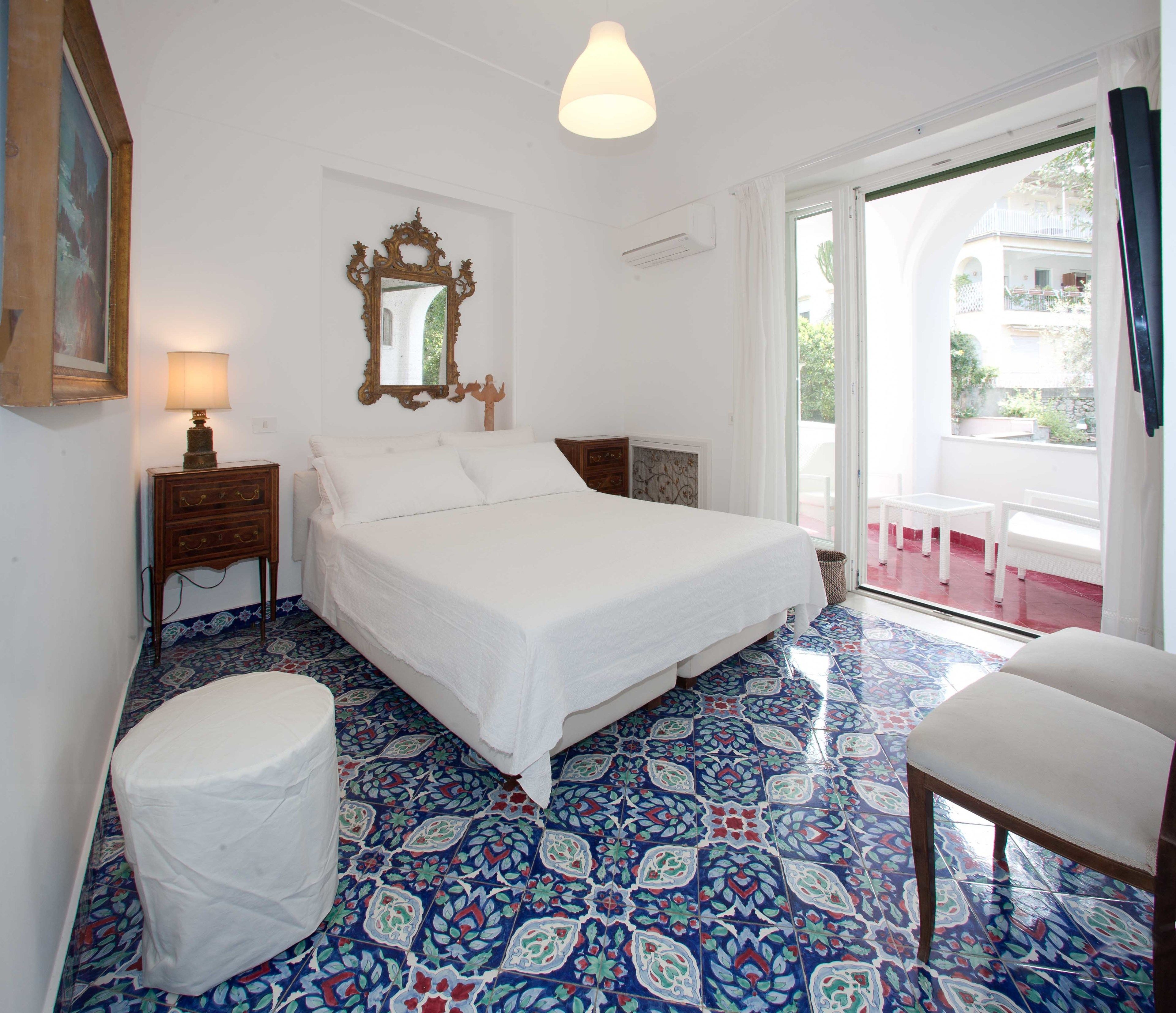 A bedroom with a bed, a nightstand, a chair, a large mirror, and a view of the outside.