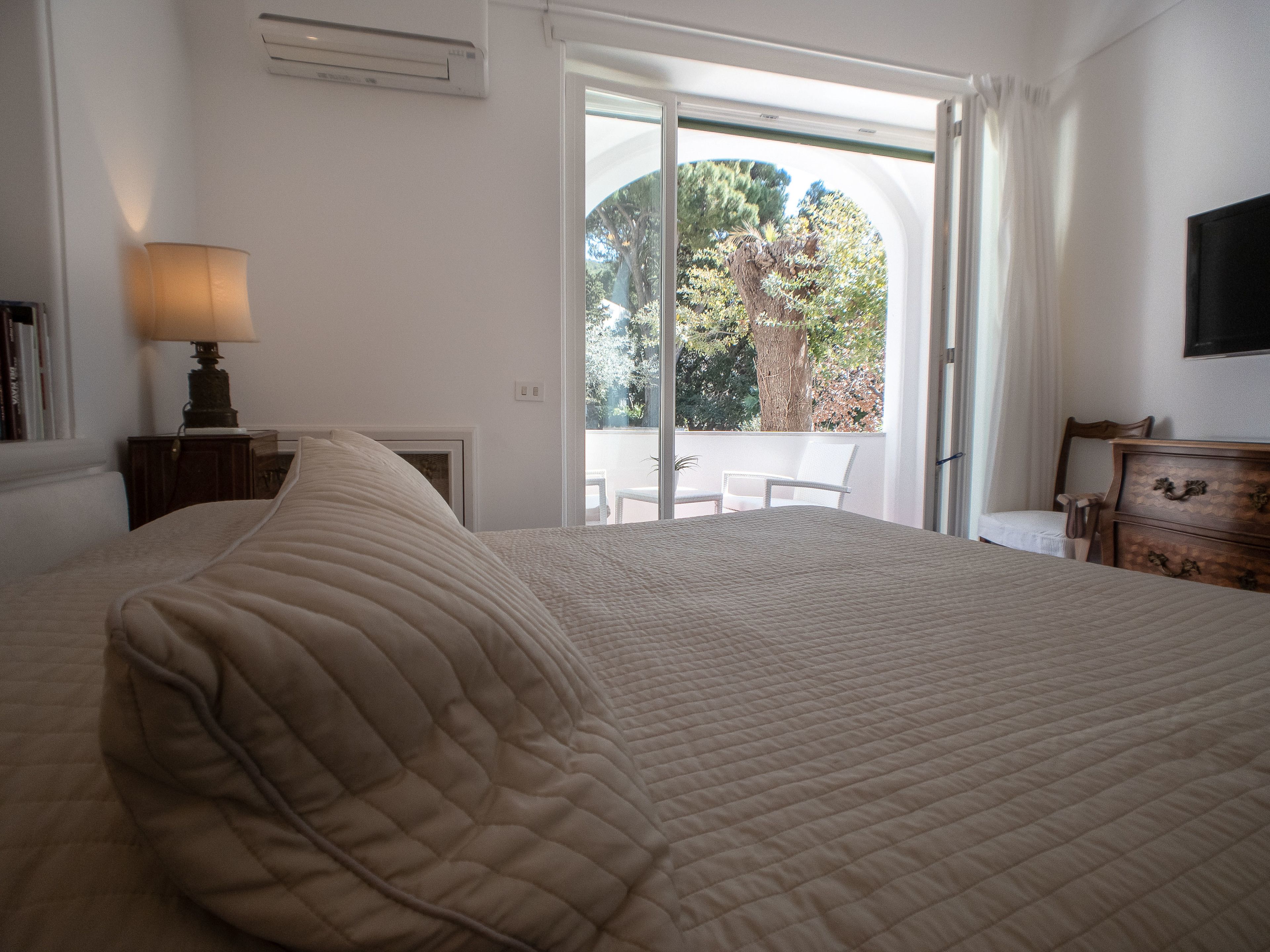 Une chambre à coucher avec un grand lit, une table de chevet avec une lampe, une commode et un téléviseur fixé au mur.
