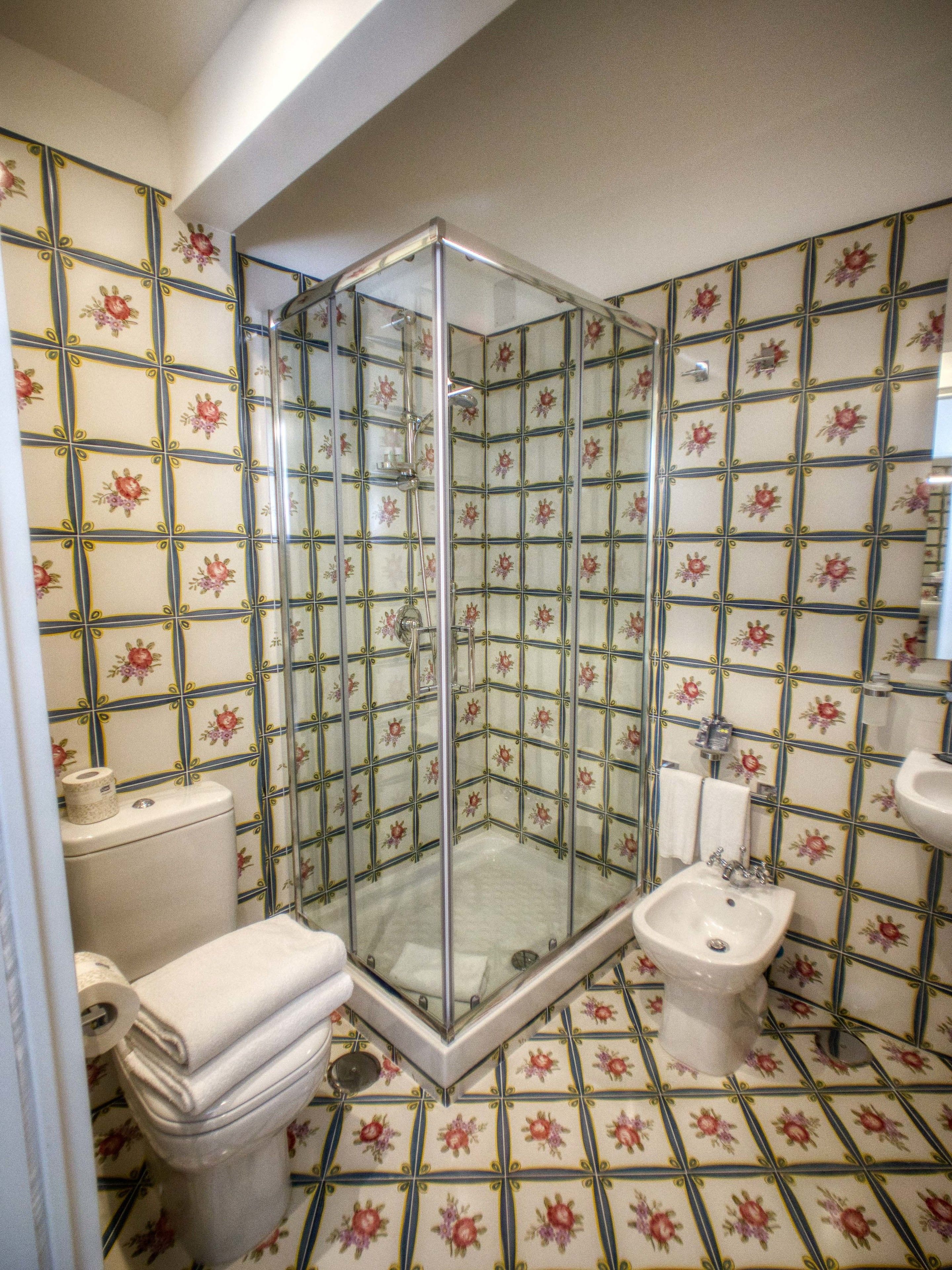 A bathroom with a shower enclosure, toilet, bidet, and tiled walls.