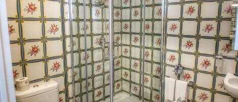 A bathroom with a shower enclosure, toilet, bidet, and tiled walls.