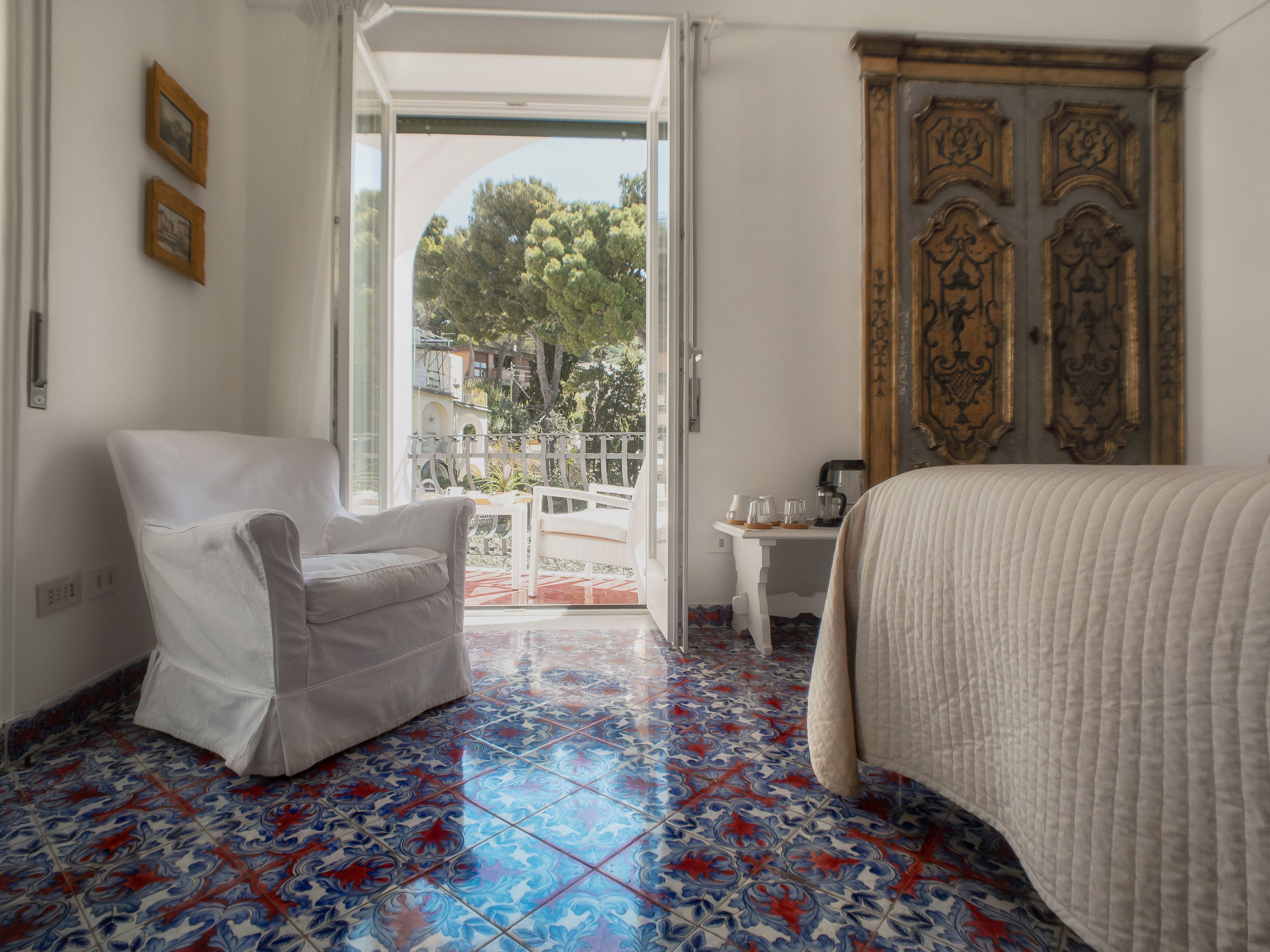 Una habitación con una cama, una silla, una mesa y vistas al exterior por una puerta abierta.