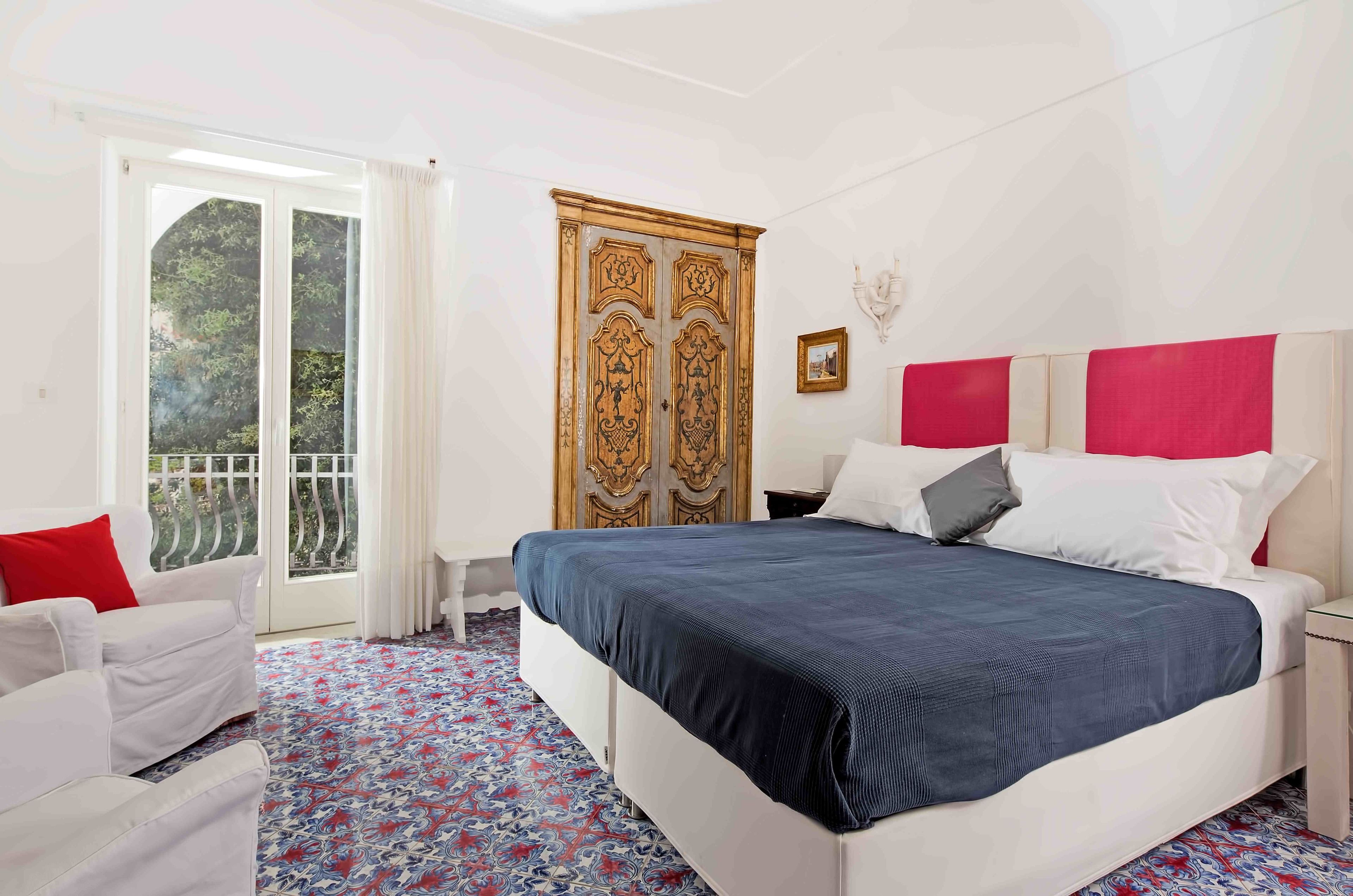 Une chambre à coucher avec un grand lit, un canapé blanc, un balcon avec une porte coulissante et une armoire en bois décorative.