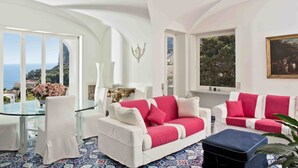 Una habitación amplia con muebles blancos, una mesa de vidrio y vistas al mar.