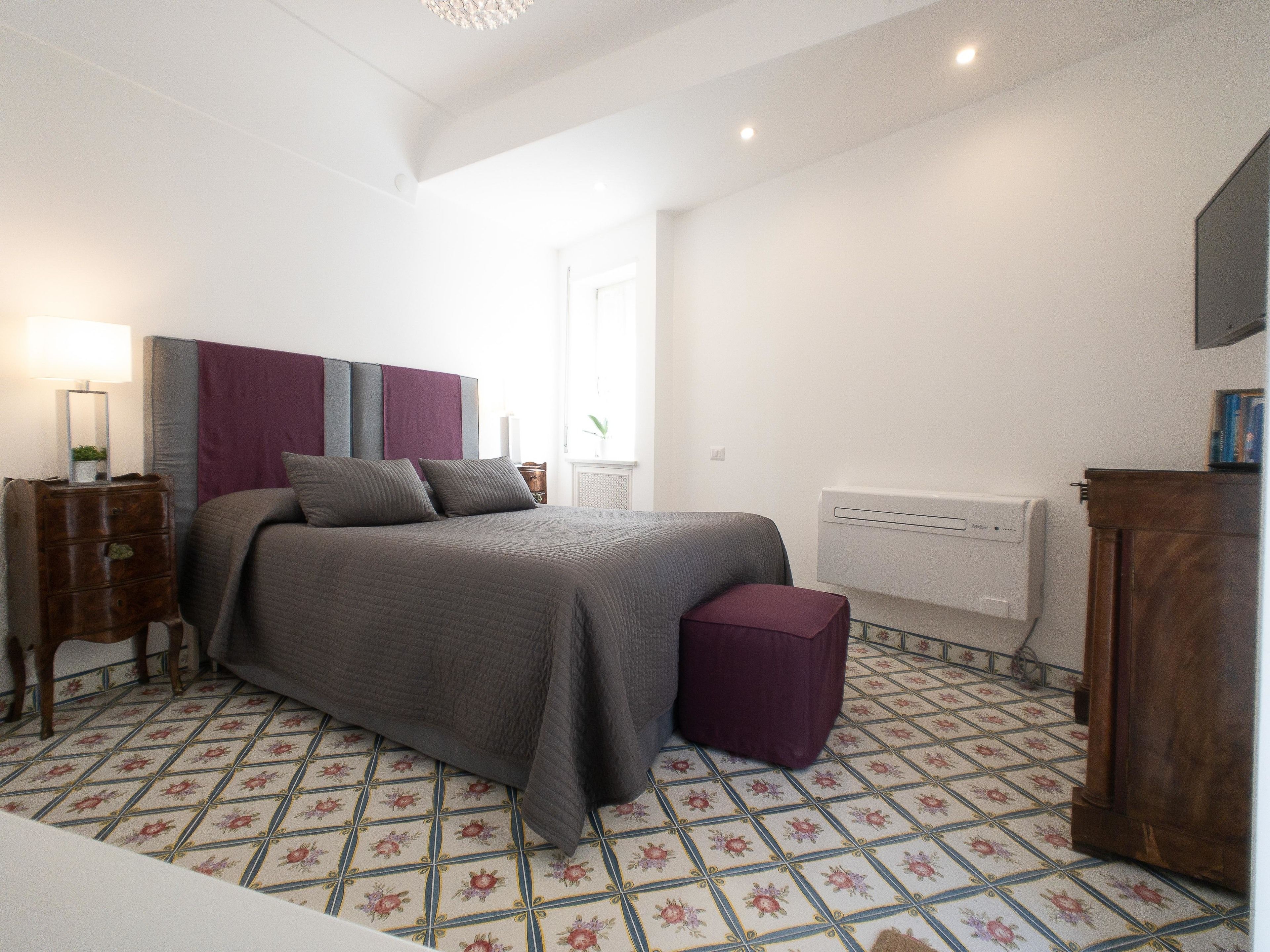 A bedroom with a bed, a nightstand, a lamp, and a radiator.