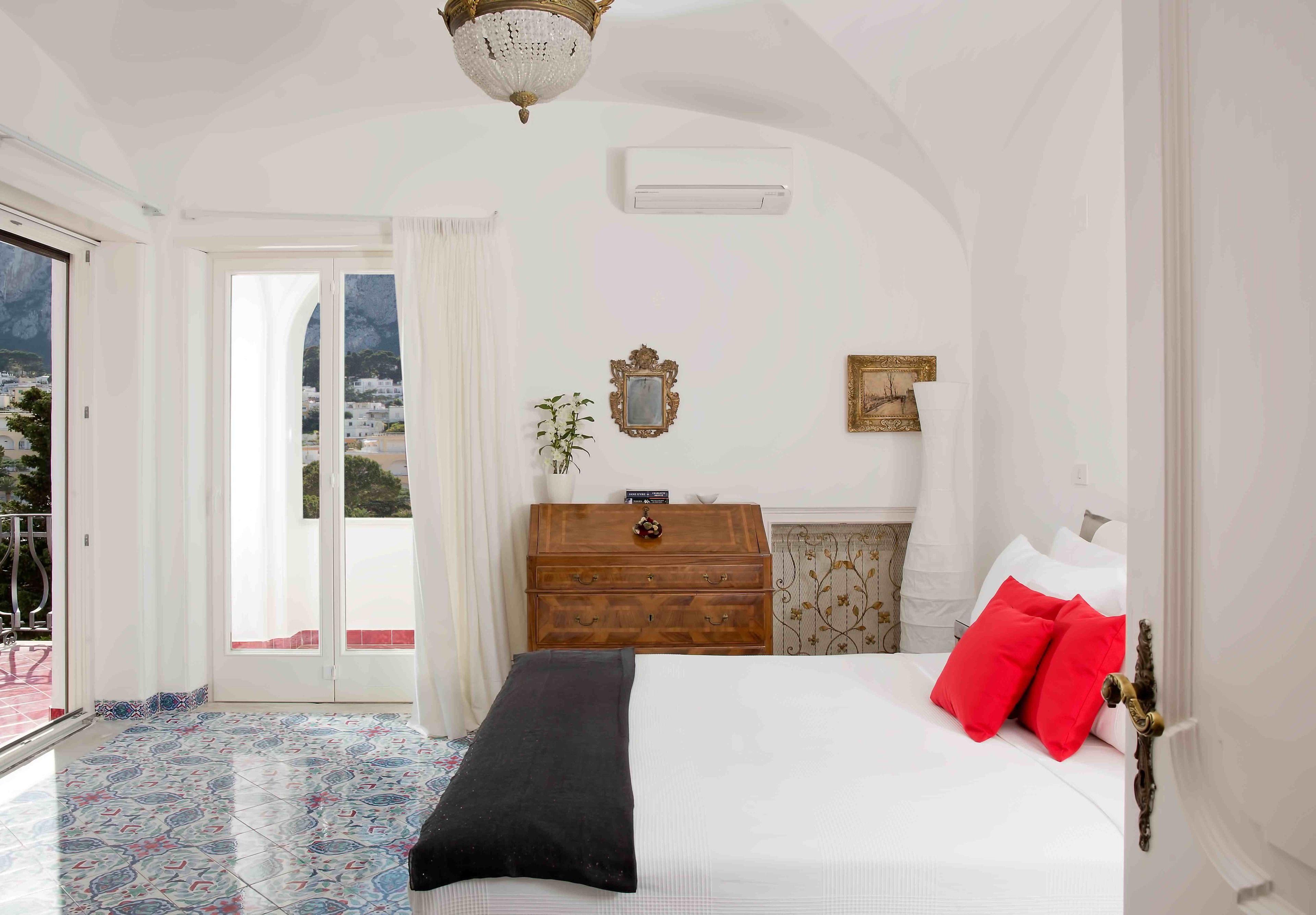 Un dormitorio con cama, cómoda, candelabro y vistas al exterior.