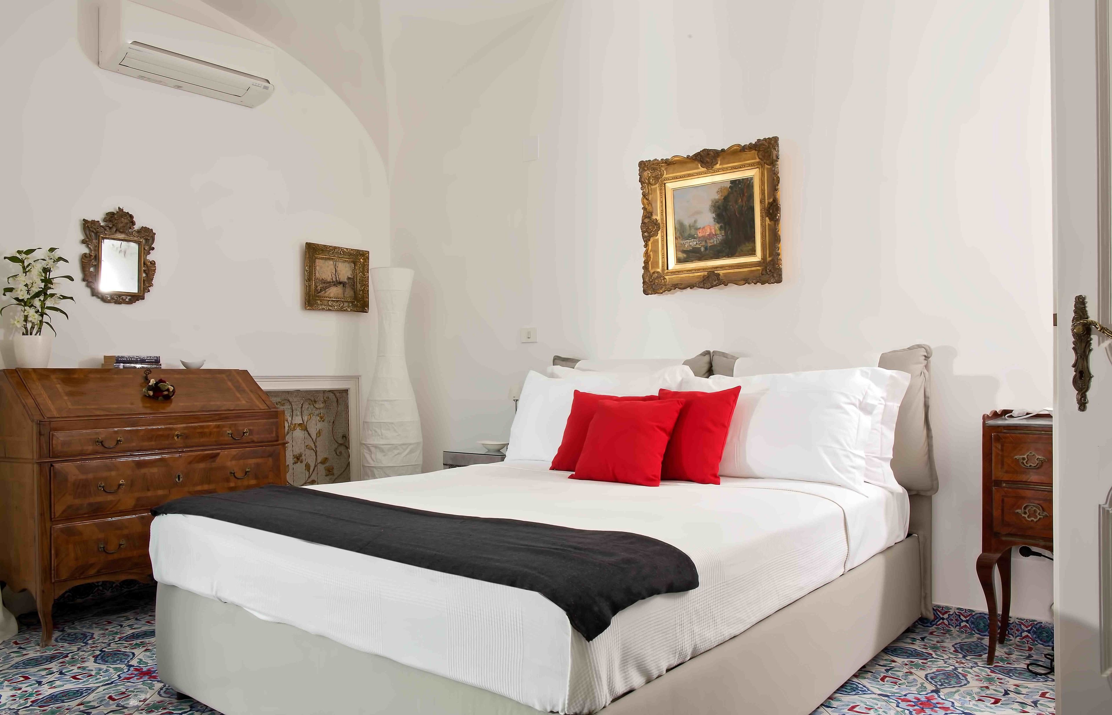 A bedroom with a large bed, a wooden dresser, a mirror, and two framed pictures on the wall.