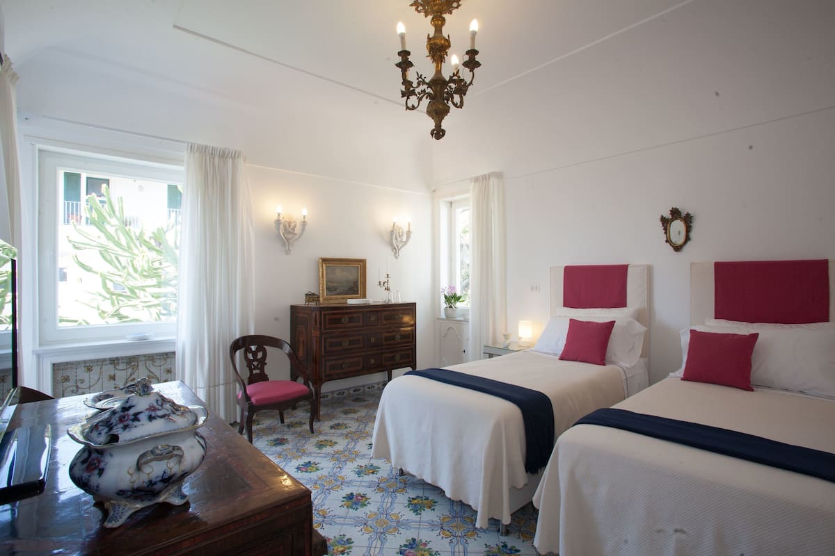 Une chambre d’hôtel avec deux lits, une commode, une chaise et un lustre.
