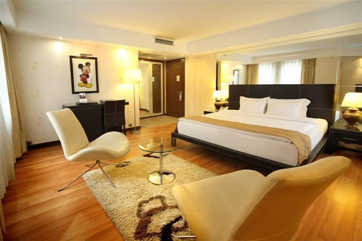 A hotel room with a large bed, a desk with a chair, a small round table, and a mirror.