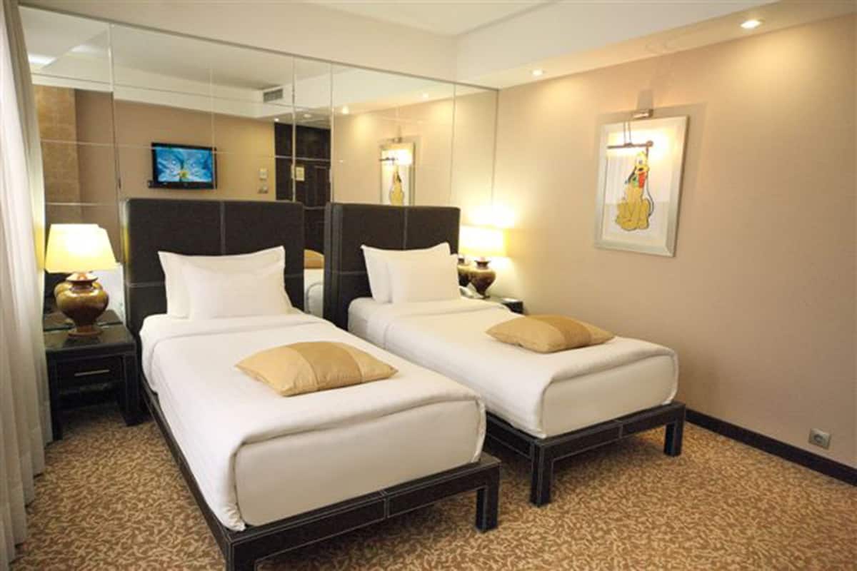 A hotel room with two single beds, a large mirror, a television, and a framed picture on the wall.