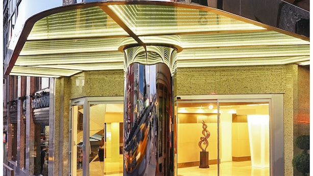 L’entrée d’un hôtel, avec une grande enseigne lumineuse sur laquelle on peut lire : « HÔTEL CARTOON ».