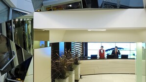 Un hall d’hôtel moderne avec un plafond au design géométrique, un comptoir d’accueil et un espace salon.