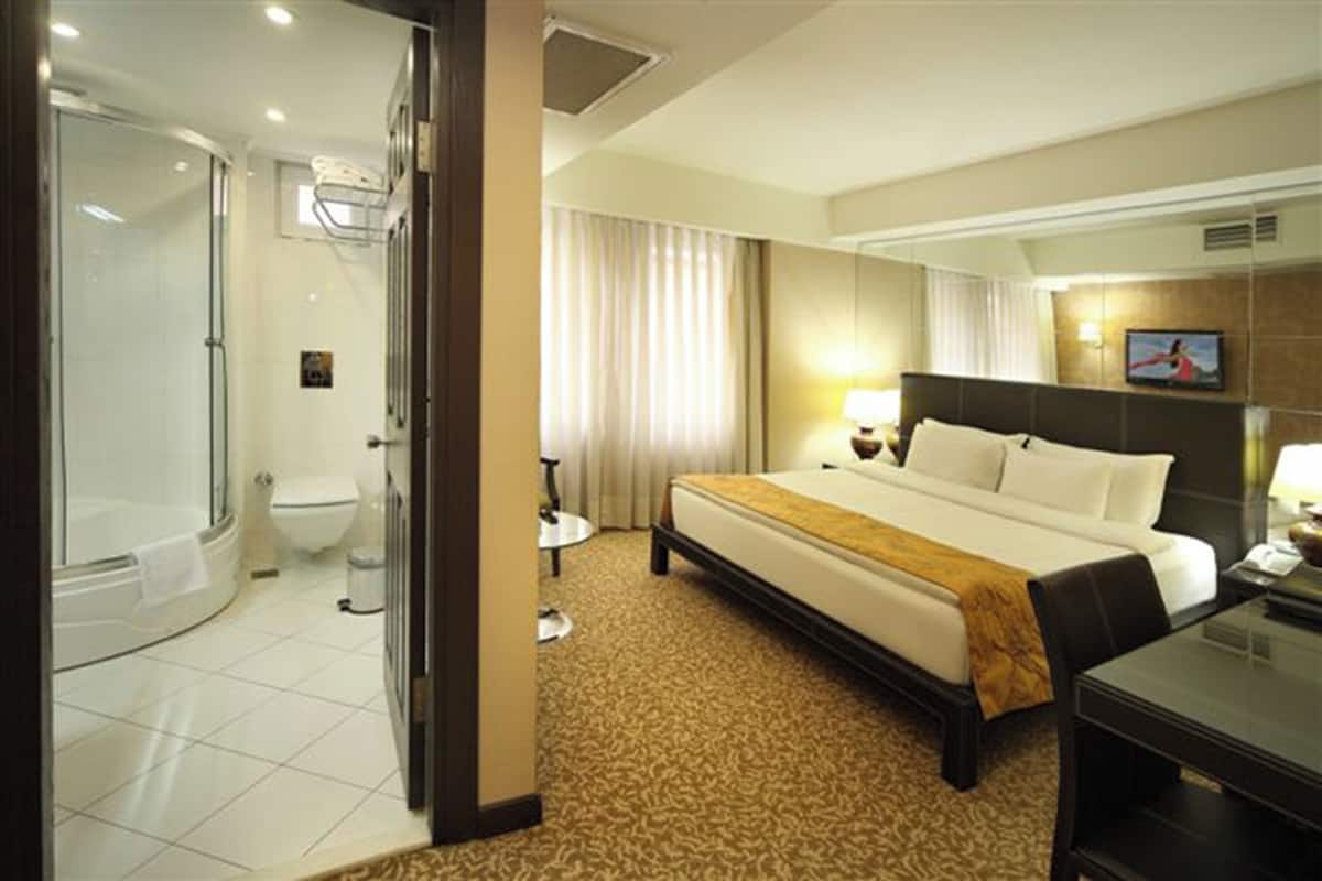A hotel room with a large bed, a separate shower area, a toilet, and a small table with a lamp.