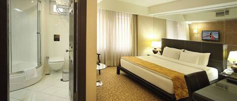 A hotel room with a large bed, a separate shower area, a toilet, and a small table with a lamp.