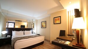 Une chambre d’hôtel avec un grand lit, des tables de chevet, un bureau, une chaise, un miroir et des œuvres d’art accrochées aux murs.