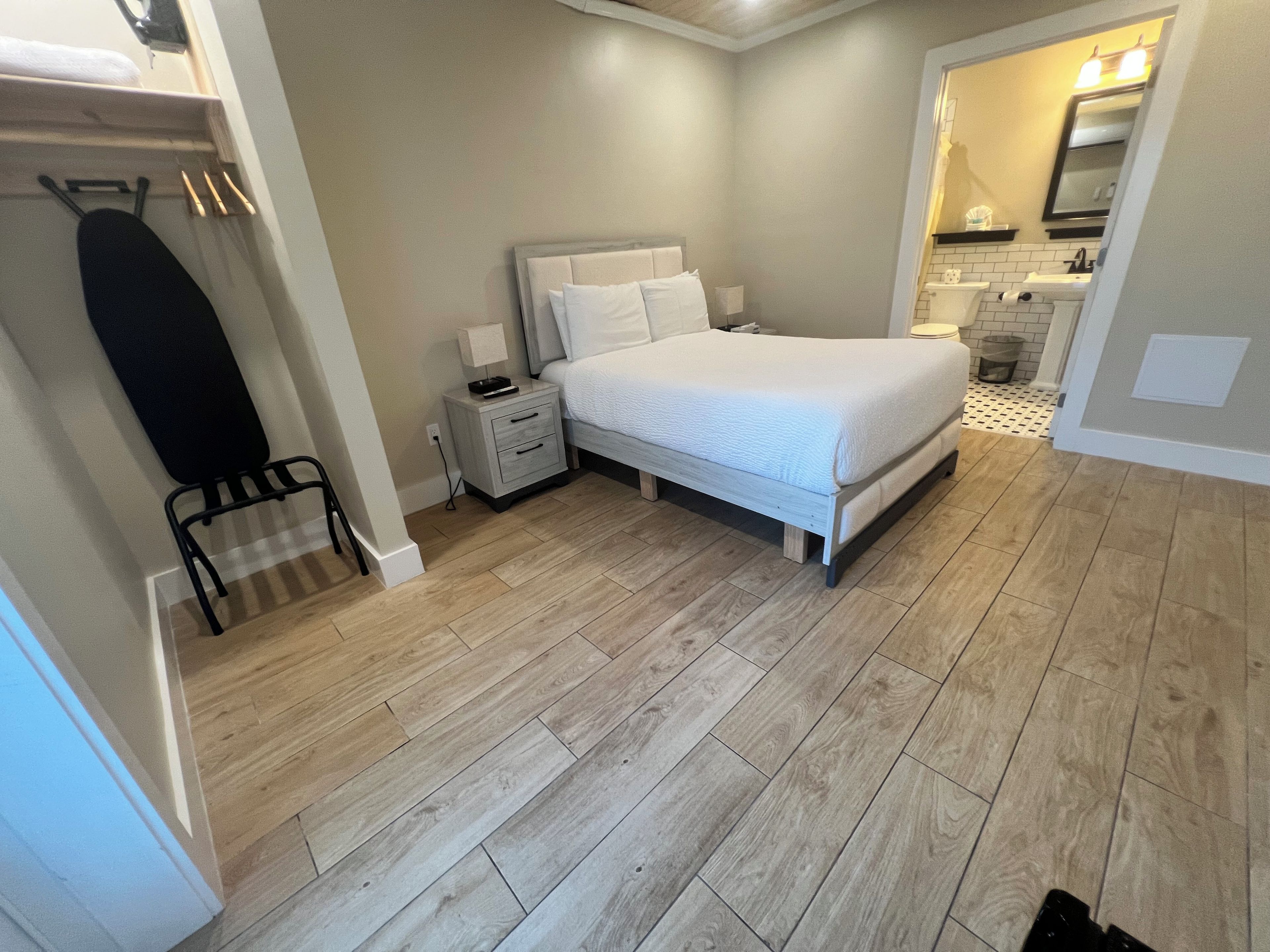 A bedroom with a bed, nightstands, a lamp, a mirror, and a bathroom with a sink and toilet.