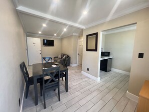 A modern living room with a dining table, chairs, a sofa, a flat-screen TV, and a kitchen area with a microwave. - Seashell Motel (Key West)