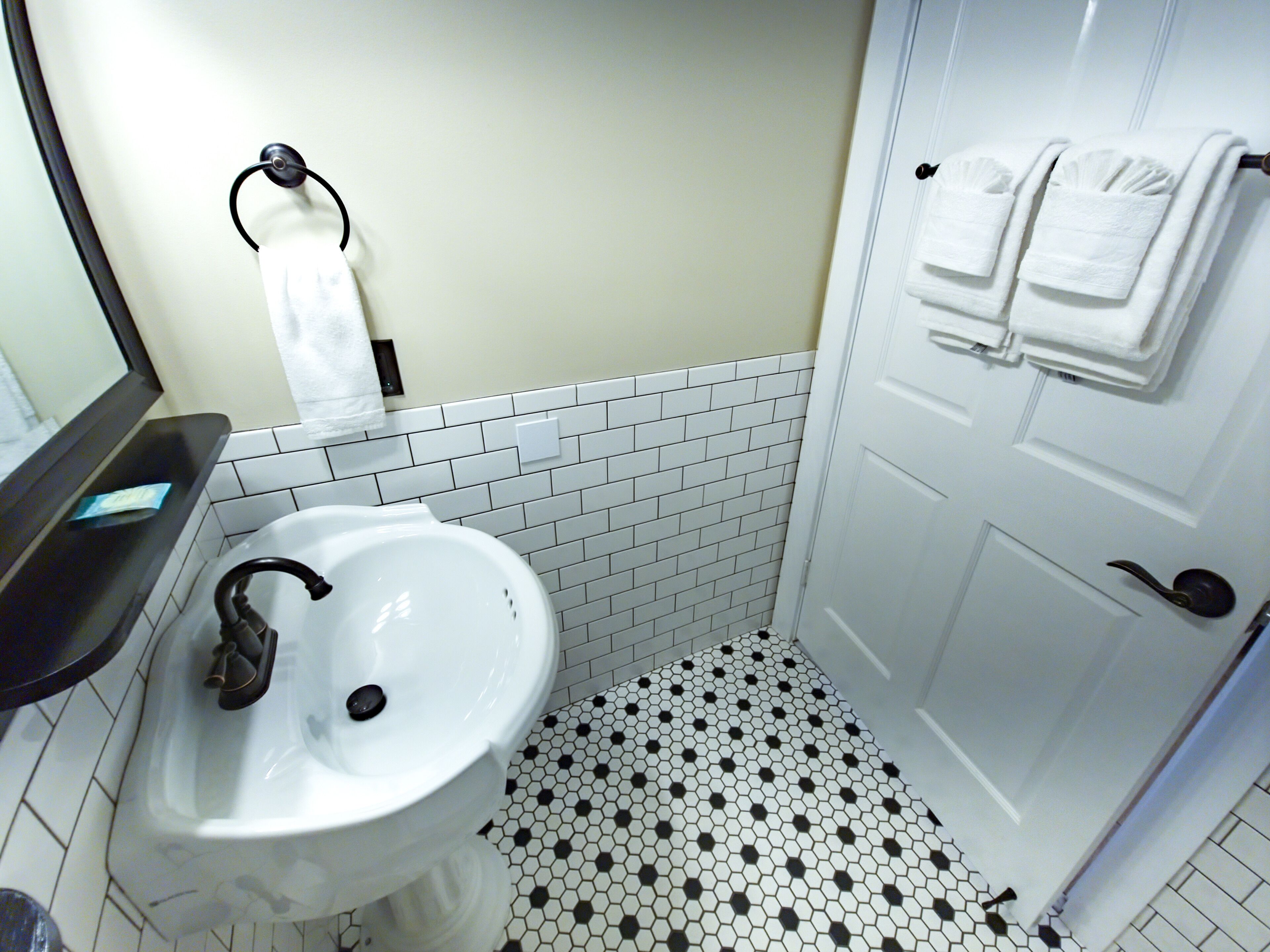A bathroom with a white sink, black and white hexagonal floor tiles, and a white door with towels hanging on it.