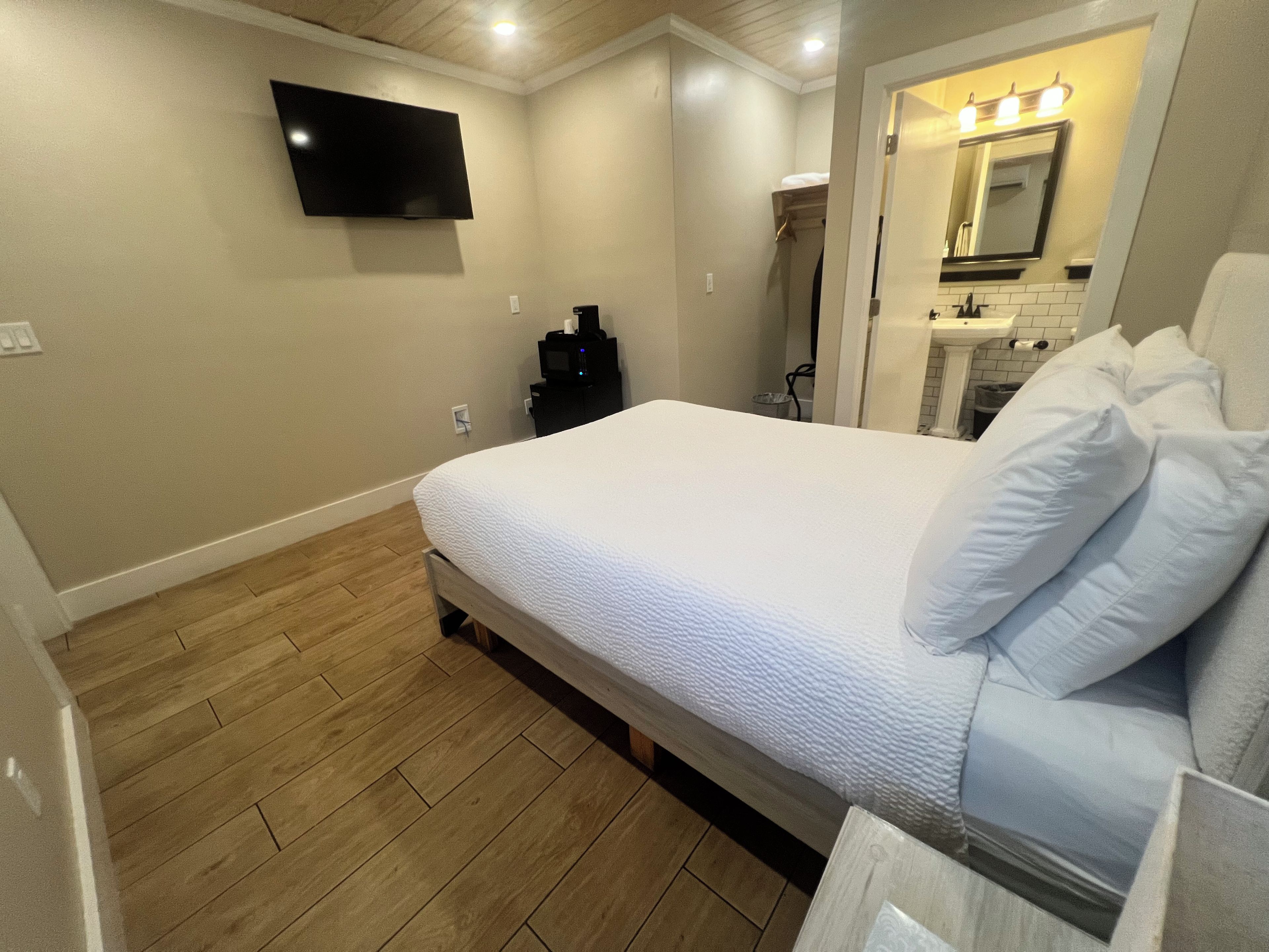 A bedroom with a bed, a television mounted on the wall, and a bathroom visible through an open door.