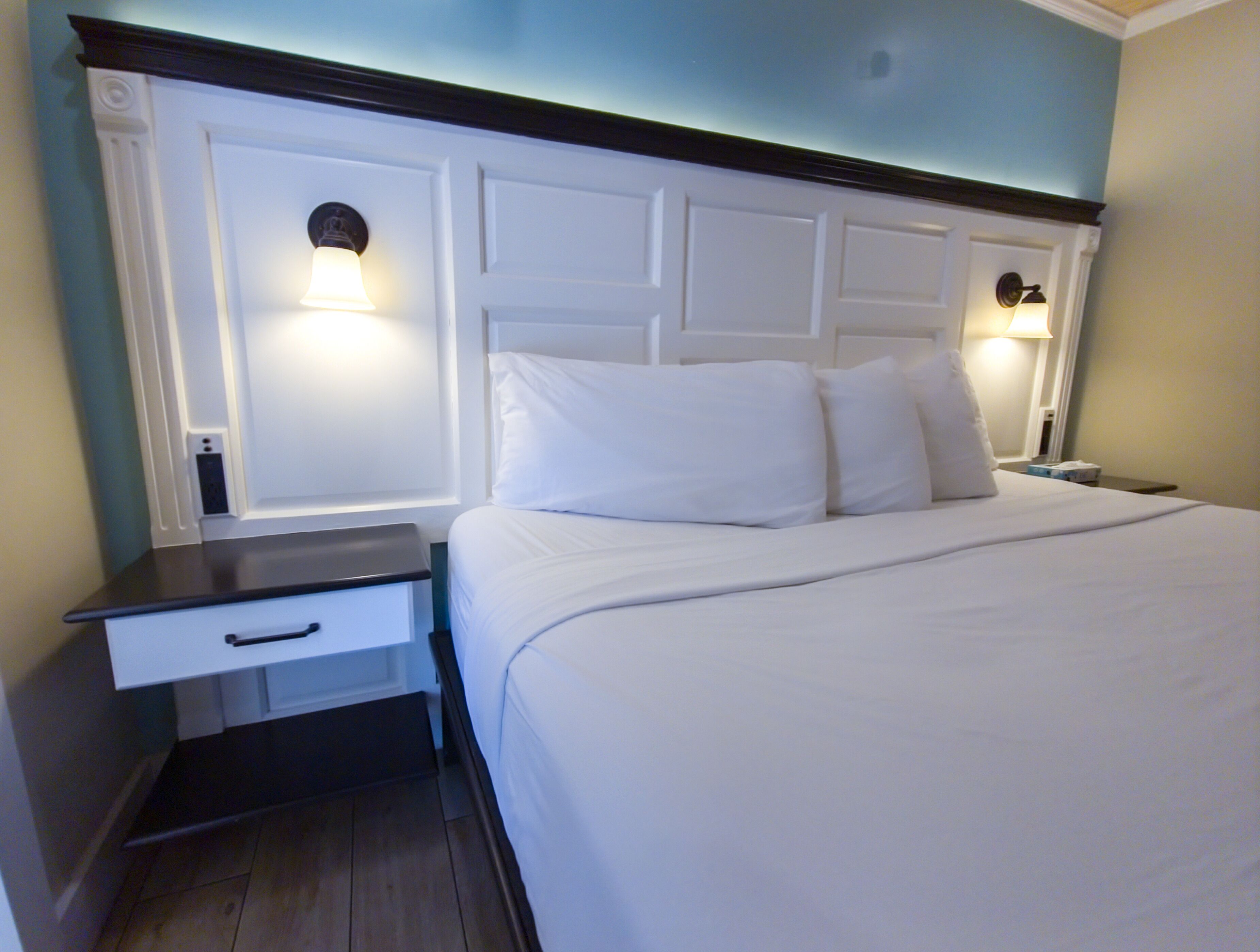 Habitació d'hotel amb un llit gran, una tauleta de nit i dues làmpades penjades a la paret.