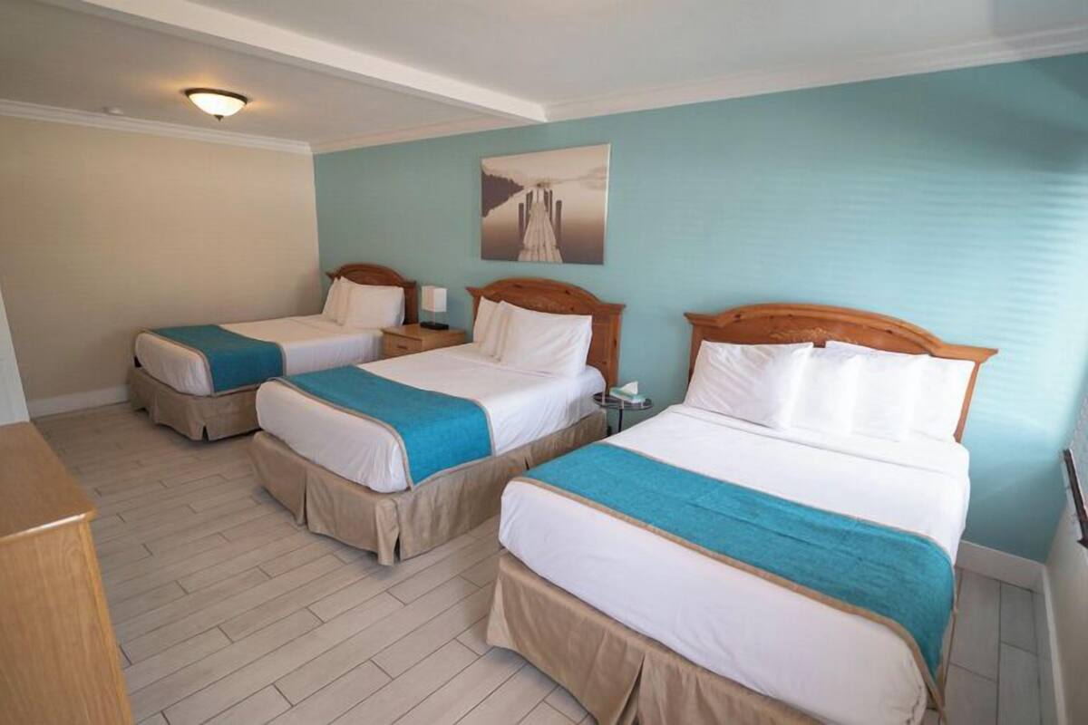 A hotel room with three single beds, a wooden desk, and a painting on the wall.