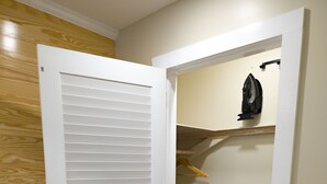 A room with a wooden floor, a white door with horizontal slats, a wooden wall, and a small shelf with a black object.