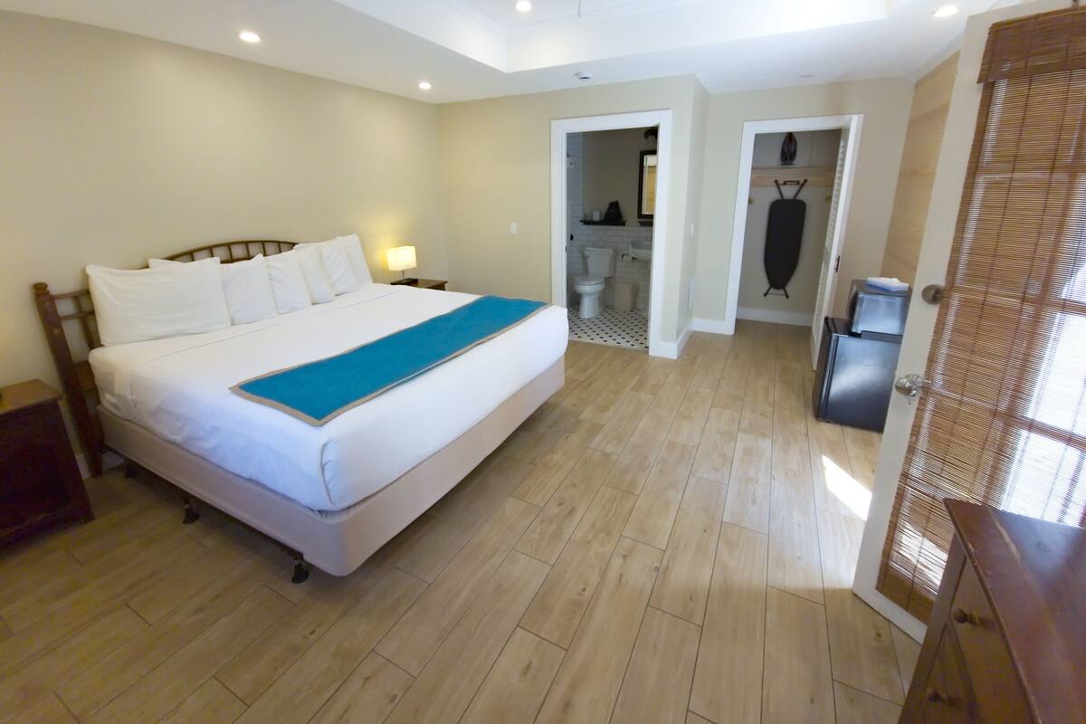 A hotel room with a bed, bedside table, lamp, and a view of the bathroom and kitchen.