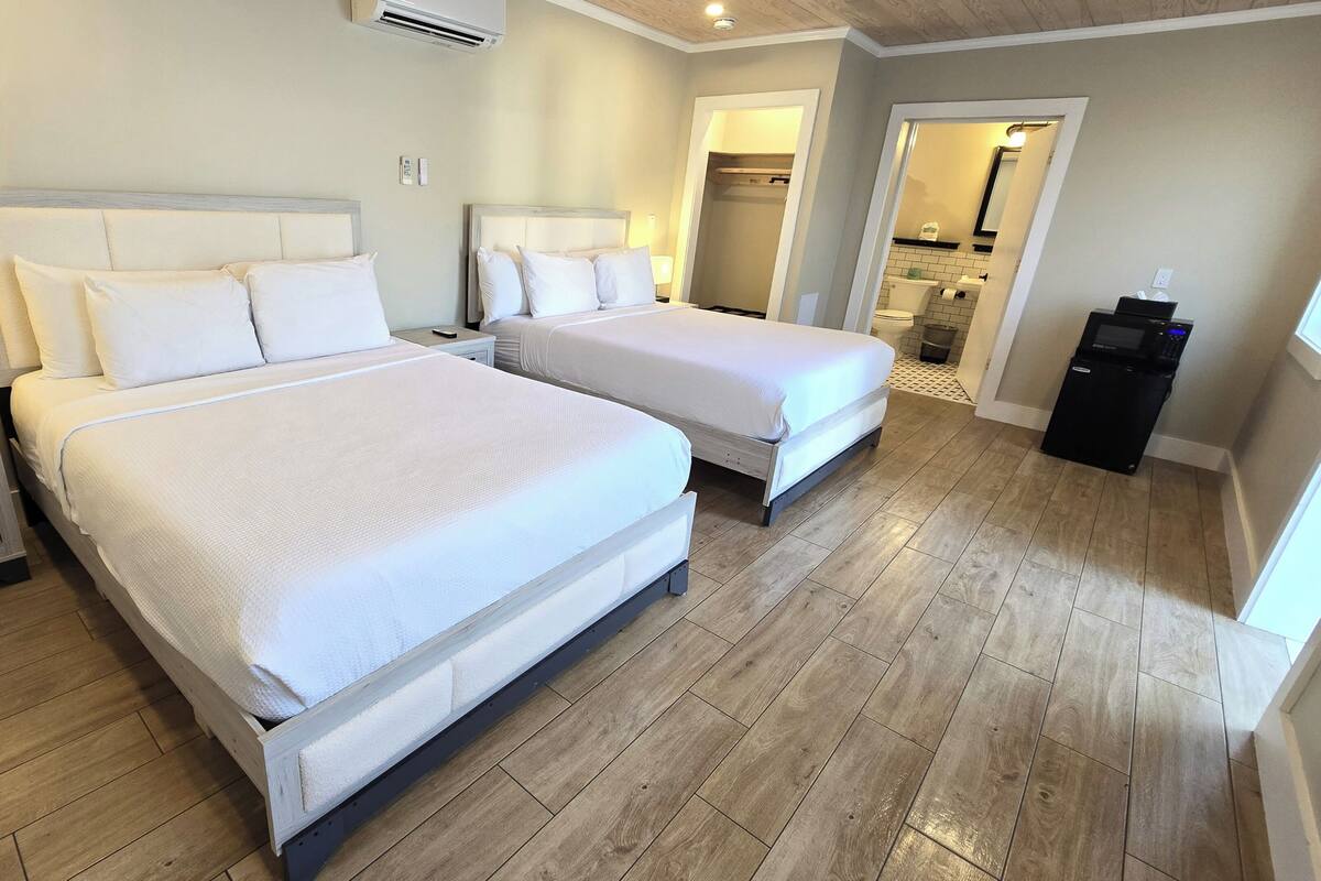 A hotel room with two beds, a bedside table with a lamp, a small desk, and a microwave.