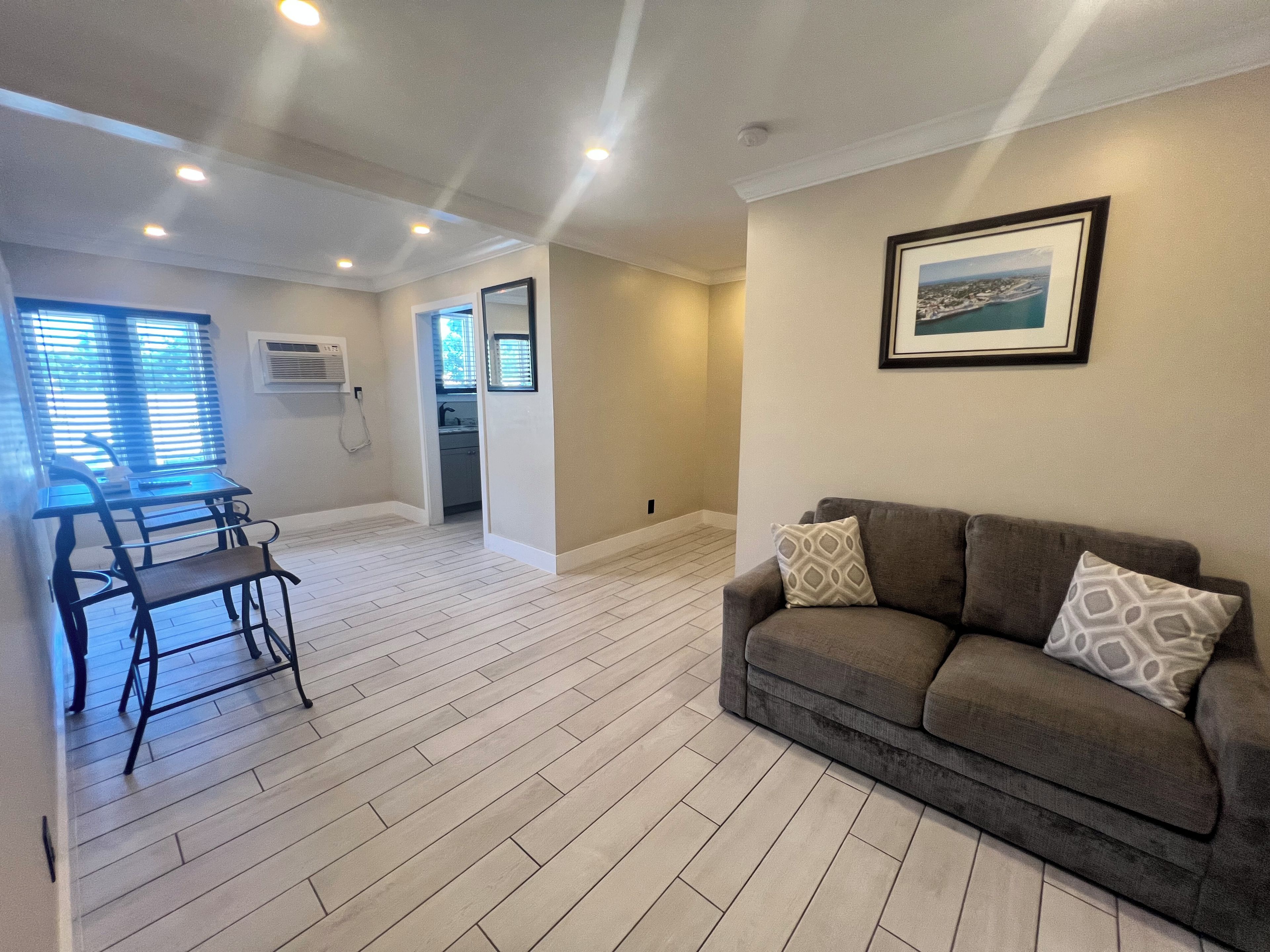 A spacious living area with a grey sofa, a dining table with chairs, and a kitchen in the background.