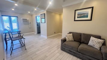 A spacious living area with a grey sofa, a dining table with chairs, and a kitchen in the background.