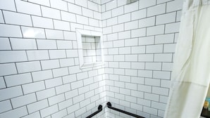 A shower with white subway tiles and a black shower curtain.