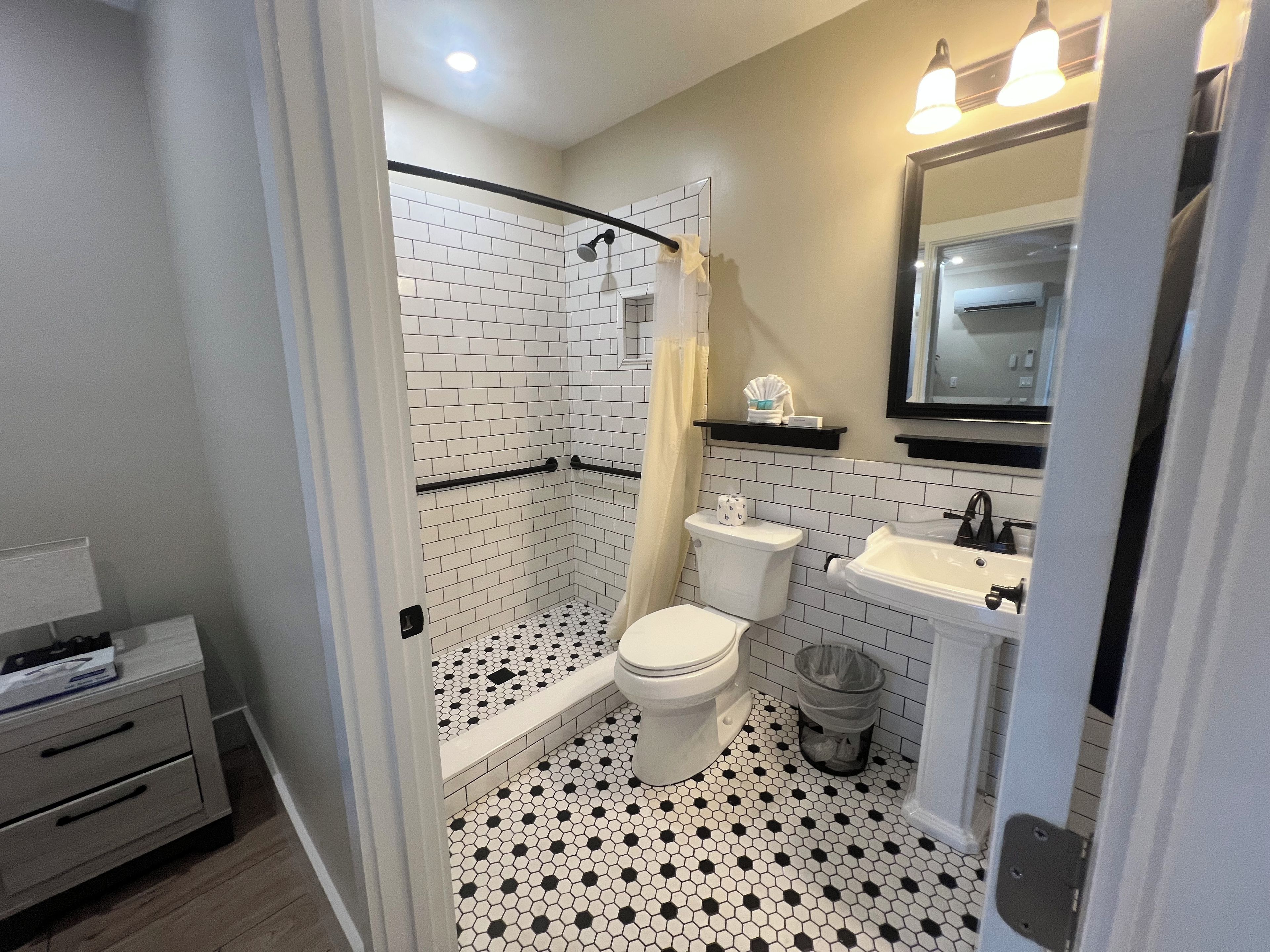 A bathroom with a shower, toilet, sink, and a mirror.