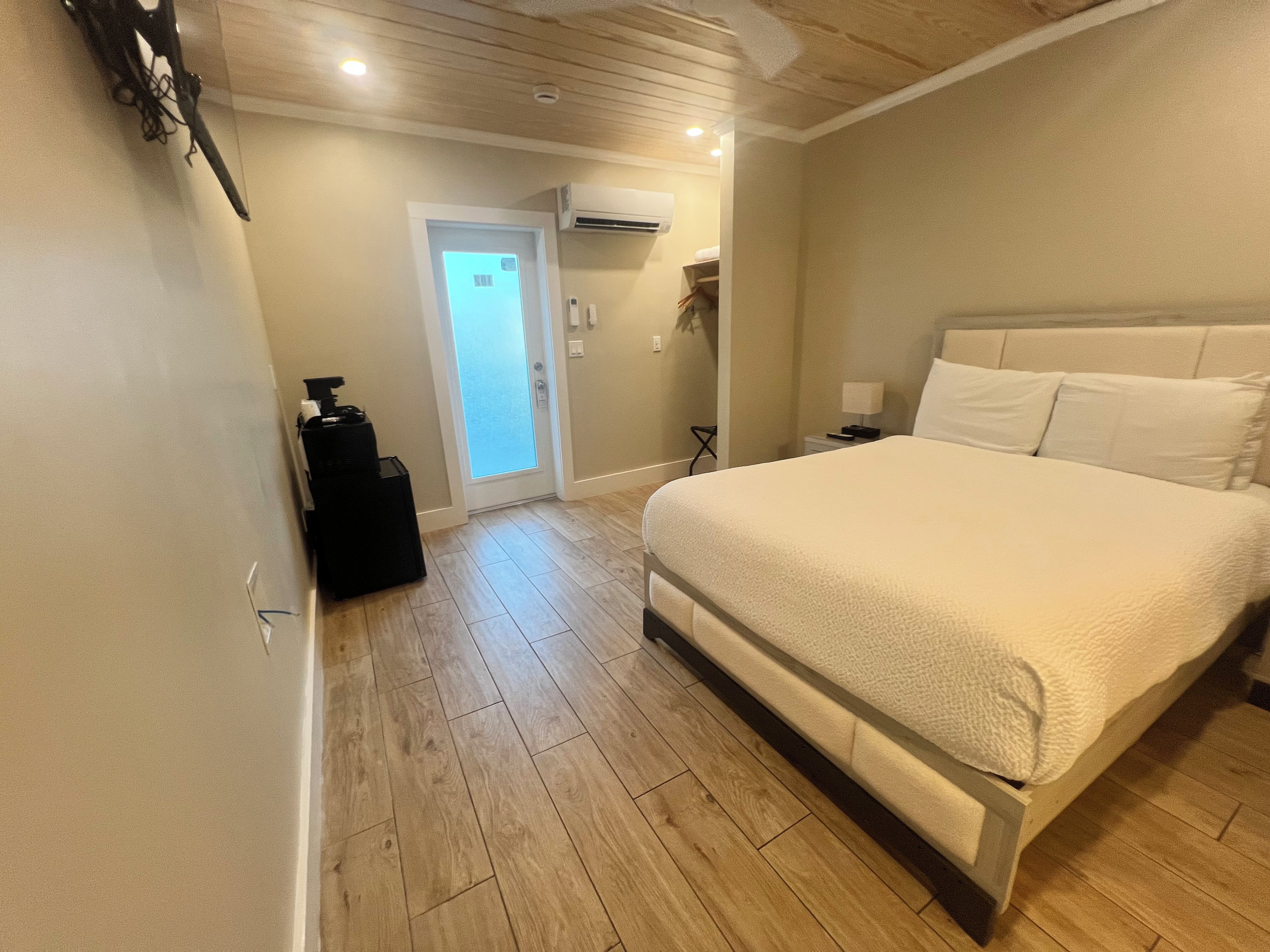 A hotel room with a large bed, a suitcase, a desk with a lamp, and an air conditioning unit.
