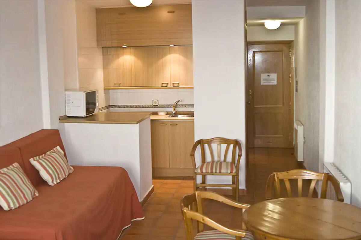 A compact room with a kitchenette, a dining area with a table and chairs, and a sofa with striped pillows.