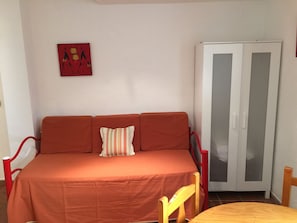 A room with a red sofa, a striped pillow, a wooden chair, and a white wardrobe with glass doors.