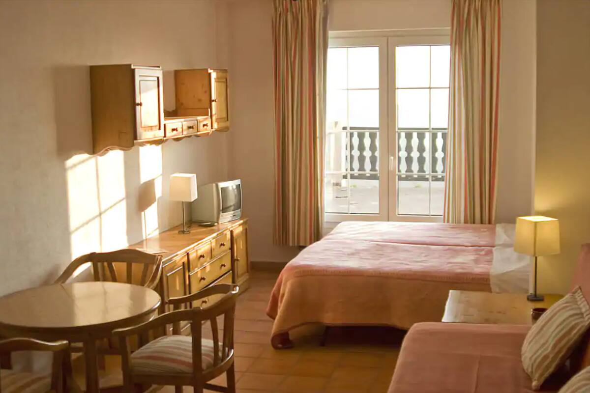 A hotel room with a bed, a desk, a chair, a television, and a balcony with curtains.